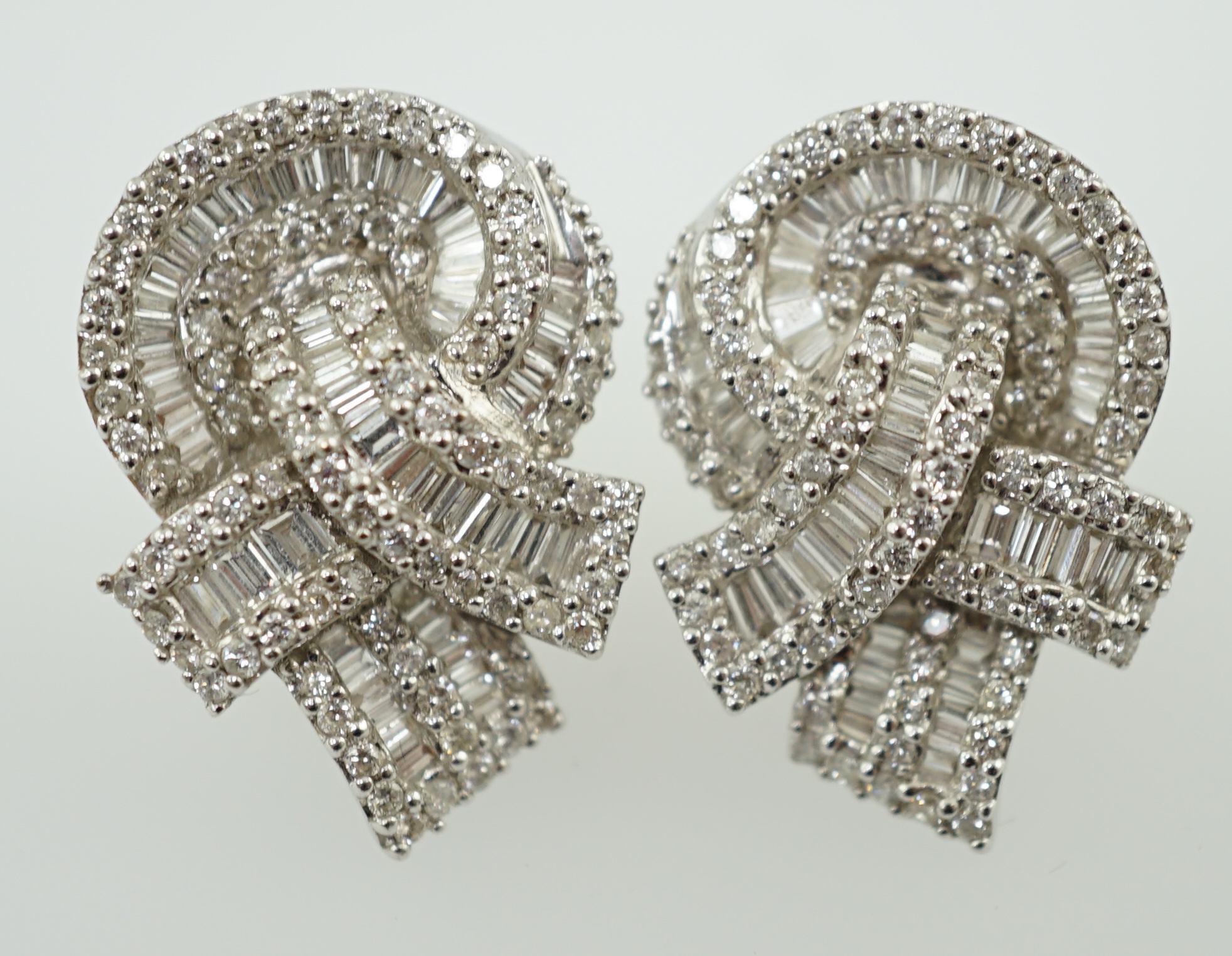 A pair of 18k white gold and pavé set round and baguette cut diamond cluster set 'knot' earrings